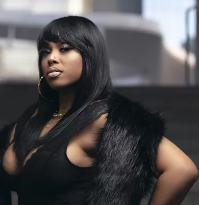 Woman in a black fur vest and hoop earrings posing on an urban stairwell