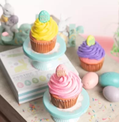 Pastel-frosted cupcakes displayed on teal stands with Easter eggs and decorations