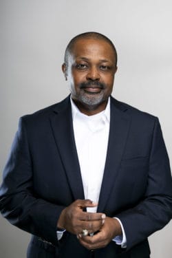 Smiling man in a navy suit and white shirt with clasped hands, posing for a professional headshot