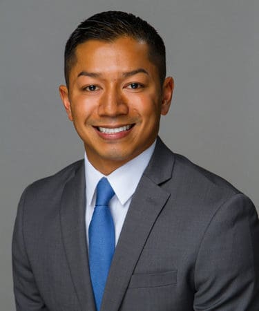 Smiling man in a gray suit and blue tie posing for a professional real estate headshot