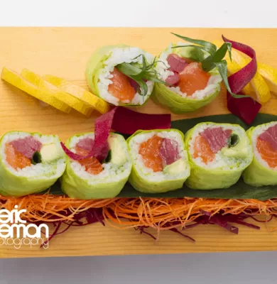 Platter of colorful sushi rolls garnished with salmon and herbs on a wooden board