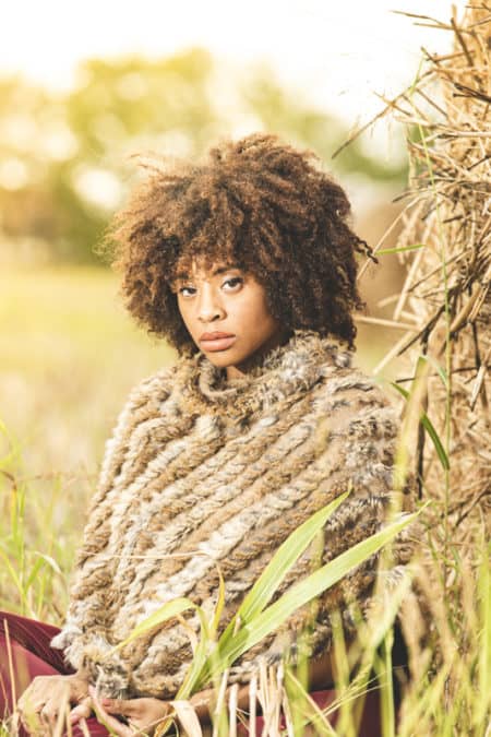 Woman with curly hair wearing a knit poncho in a field at golden hour
