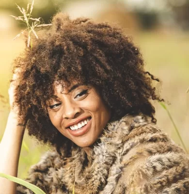 High school senior with curly hair smiling in a knit poncho in a sunlit field