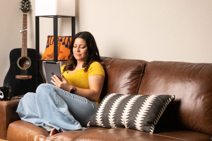 Woman sitting on a leather couch reading a tablet with a guitar in the background