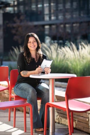 Woman smiling and writing on a tablet while seated at a red outdoor cafe table