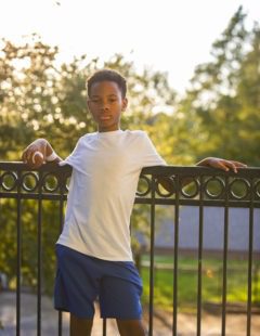 Young boy leaning against a wrought iron railing outdoors during golden hour light