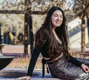 Smiling young woman in a black top and floral skirt seated near a fountain for her senior portrait