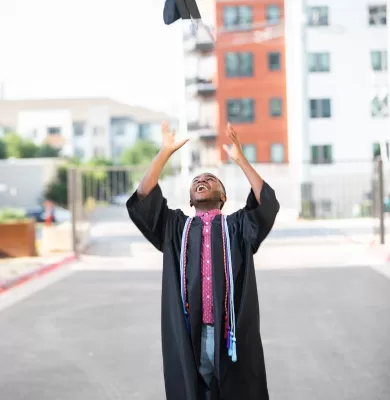 Graduate throwing their cap into the air in celebration on an Austin street
