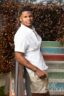 High school senior in a white shirt and khaki shorts leaning on a railing beside colorful painted stairs