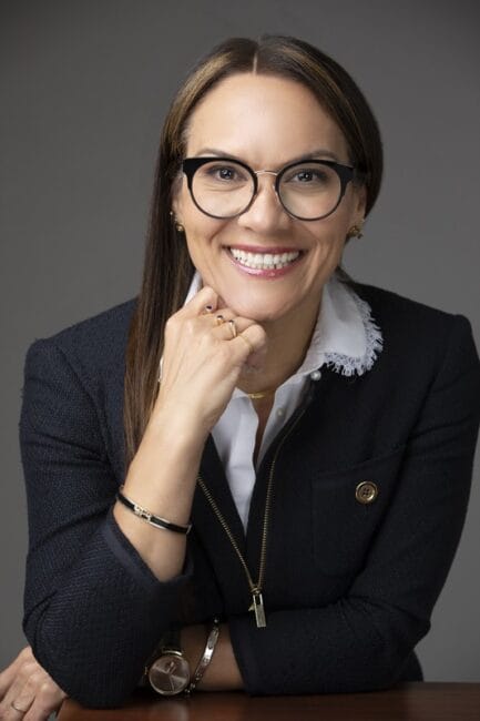 Woman in glasses and a navy blazer smiling for a professional headshot