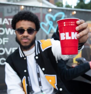 Man in sunglasses and a varsity jacket holding a branded red cup at an SXSW event