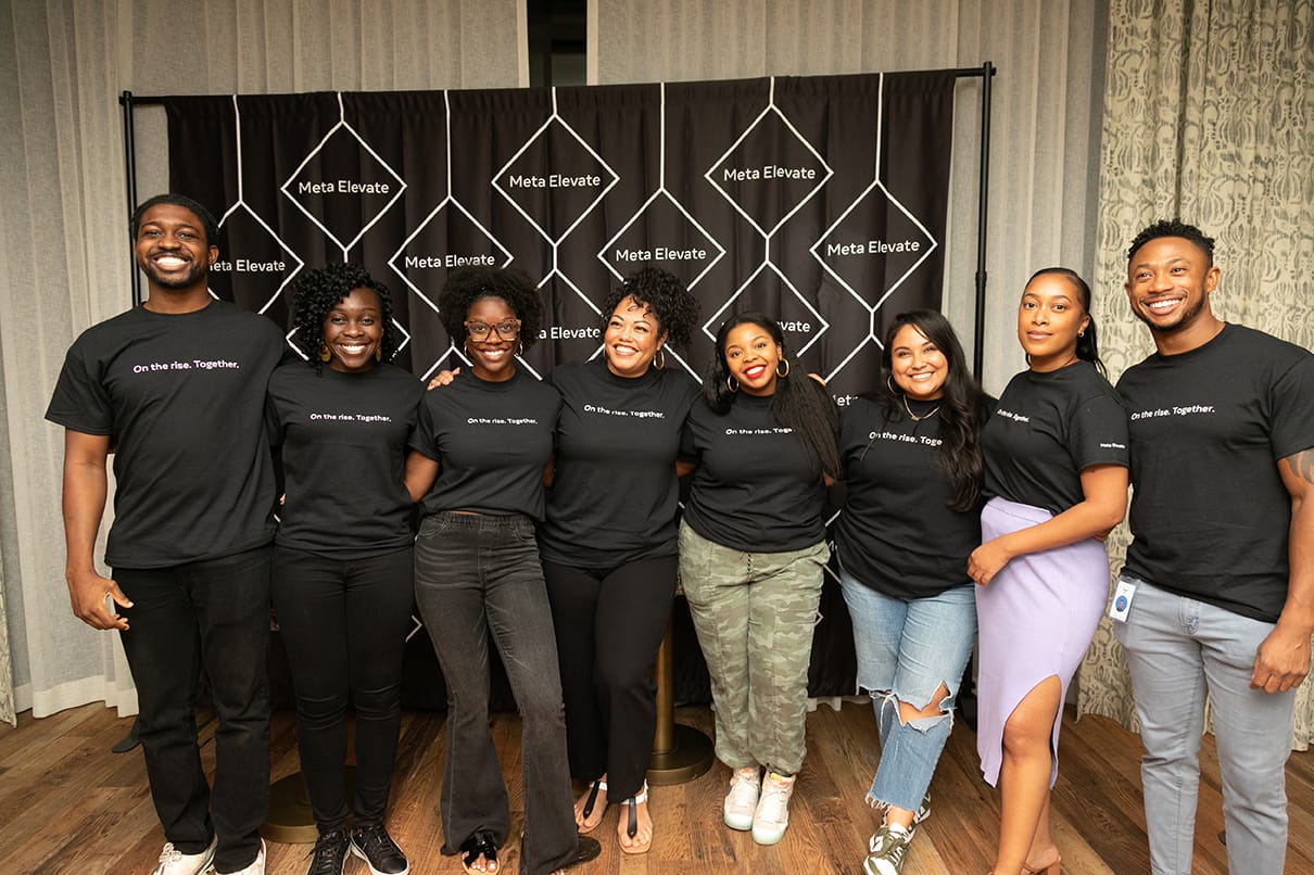 Group of eight coworkers in matching black shirts posing together at a corporate event