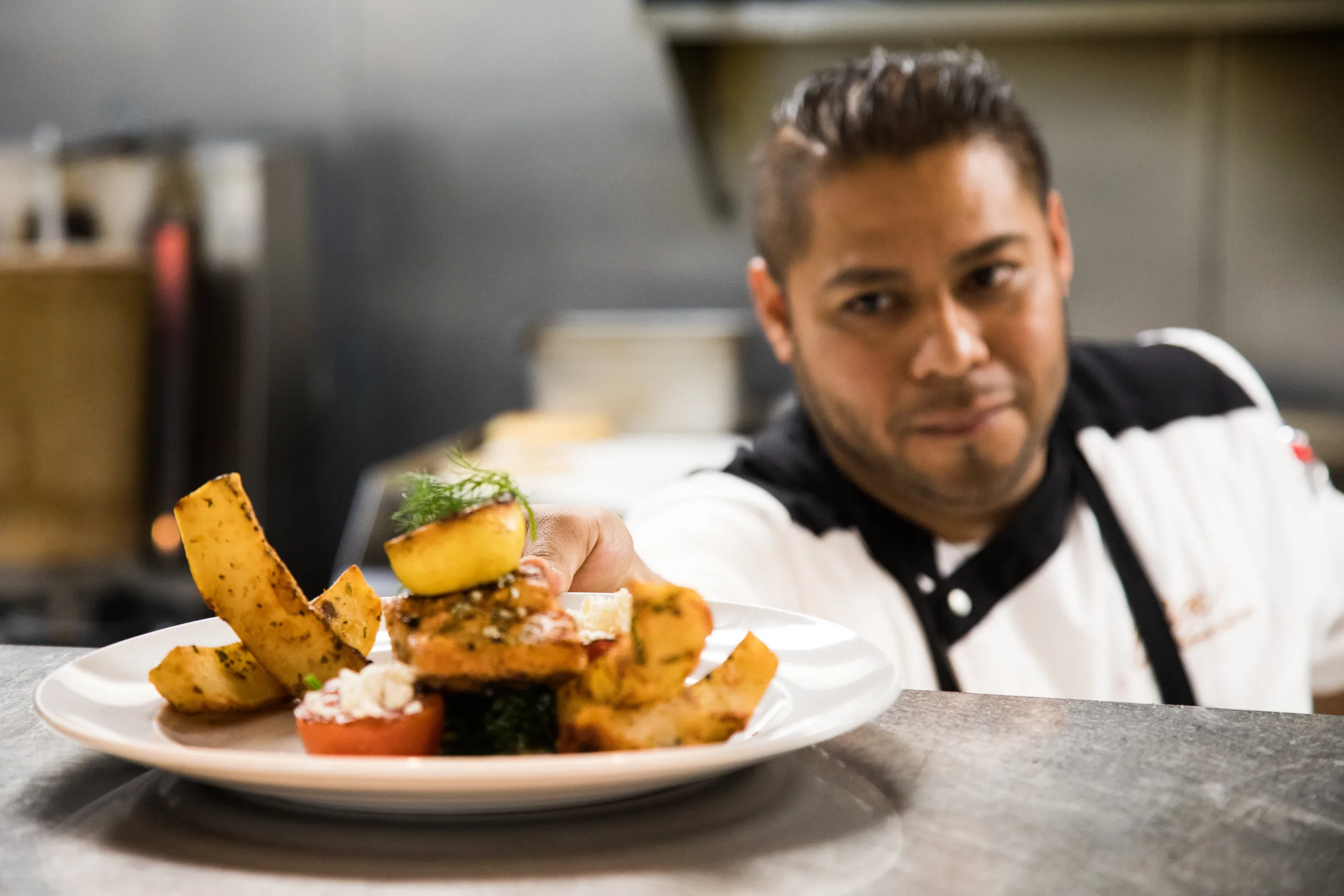 Chef presenting a plated dish of fried appetizers and salad in a restaurant kitchen