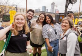 Group of attendees with name badges smiling together at a SXSW networking event with the Austin skyline behind them