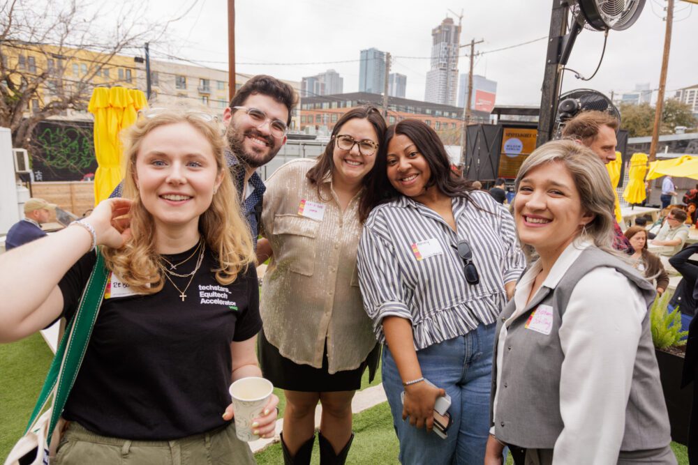 Group of attendees with name badges smiling together at a SXSW networking event with the Austin skyline behind them