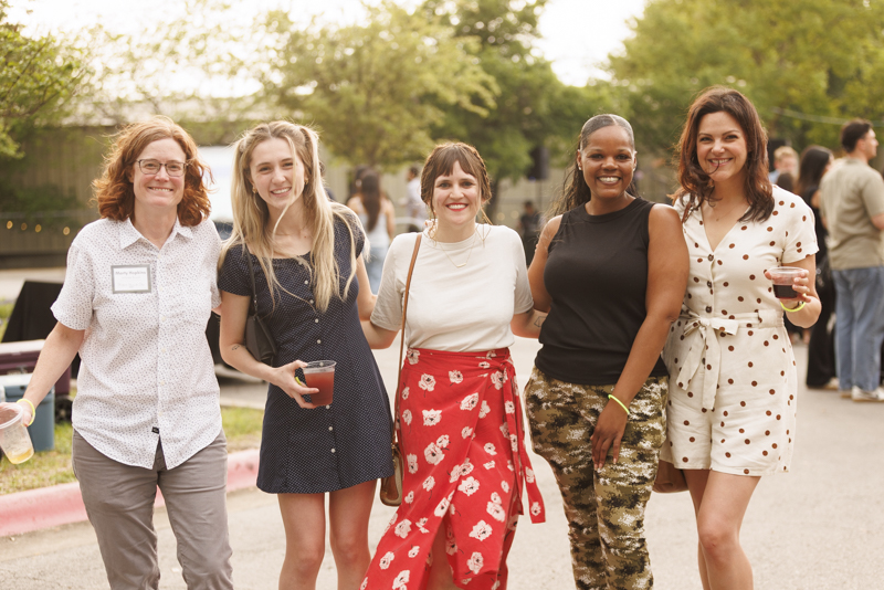 Five women smiling and laughing together outdoors at an Austin corporate event