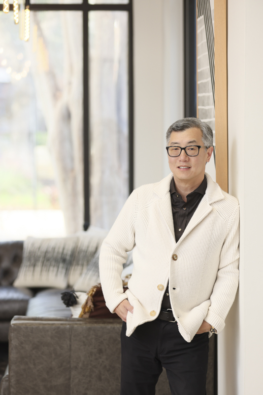 Smiling executive in glasses and a white cardigan standing indoors near a window for the Hyper Equity brand photography case study