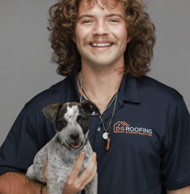 Smiling man with curly hair and mustache in a DG Roofing & Construction polo shirt holding a puppy, Austin branding headshot