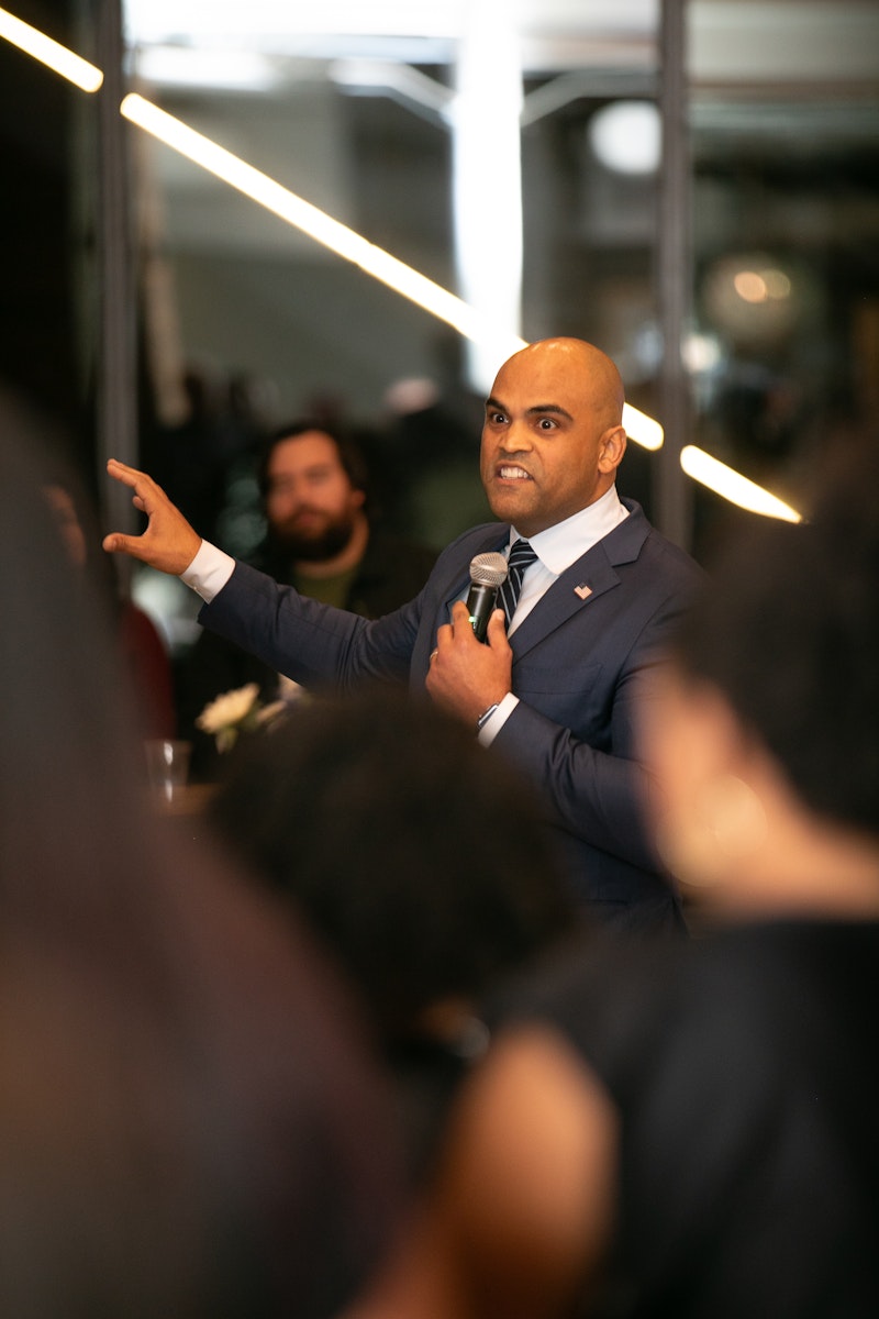 Man in a suit speaking into a microphone while addressing an audience at a corporate event