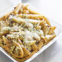 Garlic parmesan fries topped with herbs in a white to-go container