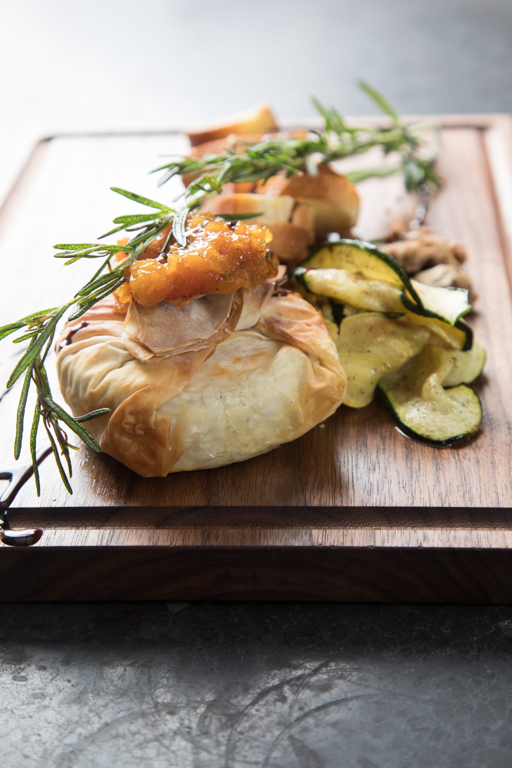 Baked phyllo pastry appetizer garnished with fresh rosemary, plated on a wooden board with roasted zucchini