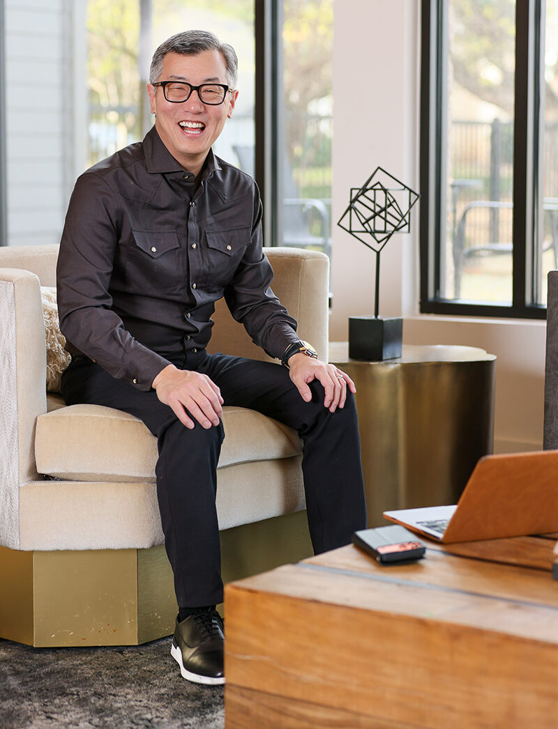 Man in a dark button-up shirt smiling while seated in a modern living room