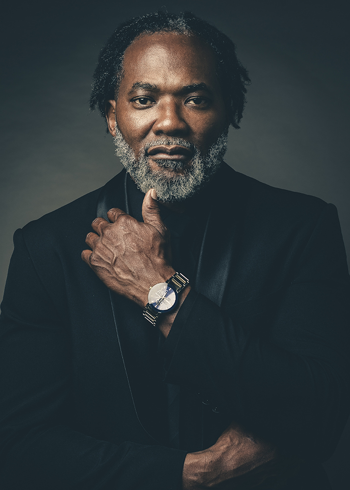 Distinguished older man with a gray beard in a black suit posing in a dramatic studio portrait