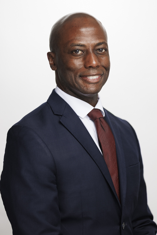 Man in a navy suit and maroon tie smiling for a professional headshot on a white background